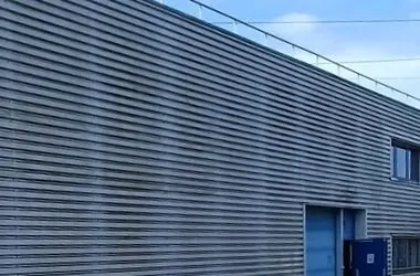 Avant : bardage métallique gris encrassé sur un bâtiment commercial